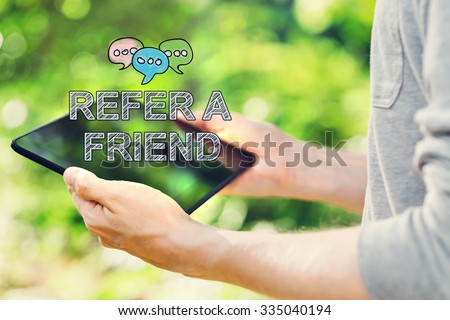 Refer A Friend concept with young man holding his tablet computer outside in the park
