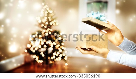 Female hand opening a gift box by a Christmas tree in a room