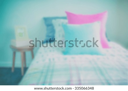 blur image of Light blue and pink pillow on sweet bedding and picture frame on bedside table