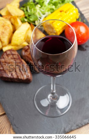 Red wine glass and steak with grilled potato, corn, salad on stone plate