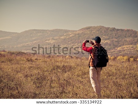 Male tourist with backpack taking pictures of the autumn scenery to your smartphone.
