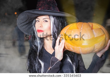 Halloween! Horror and magic holiday night. Pretty young woman dressed in witch fancy dress. Holiday makeup. Girl holding carved pumpkin with devil light