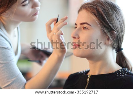  young makeup master looking at woman`s makeup in salon