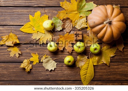 Apples and gift with pumpkin and leafs on wooden table.