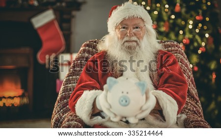 Smiling santa offering piggy bank at home in the living room