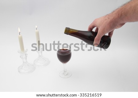Human hand pours a glass of wine Kiddush the Shabbat, Shabbat candles Shabbat according to a table with a white tablecloth.