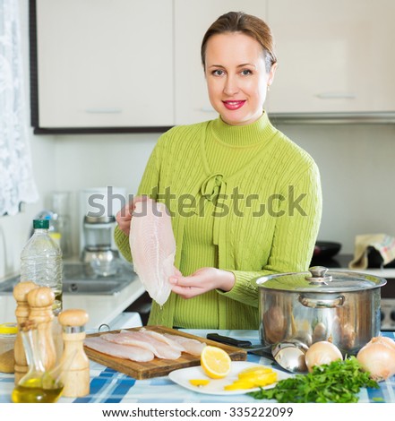 Smiling young housewife cooking soup with filleted fish at kitchen