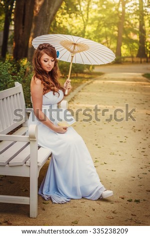 Beautiful bride in the Park with a white umbrella and a fan