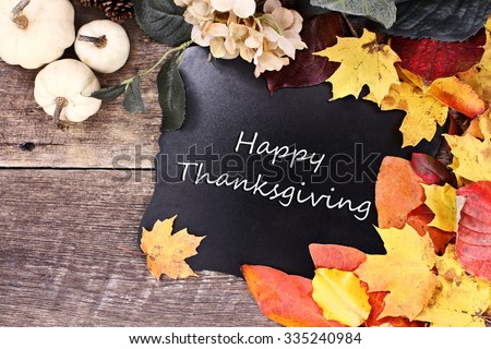 Chalk board with text Happy Thanksgiving surrounded by autumn leaves, flowers and white pumpkins over a rustic background.