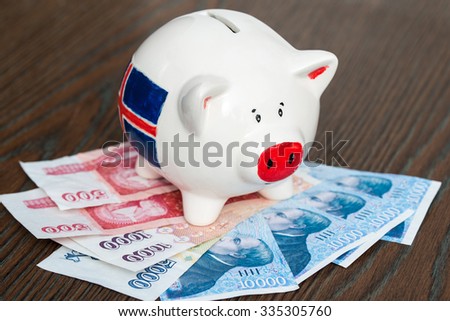 Piggy bank with Icelandic flag on icelandic bills, wooden background