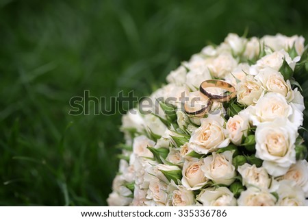 Closeup view of one beautiful fresh bright white yellow big wedding bouquet of rose flowers with gold rings lying on green grass sunny day outdoor on natural background, horizontal picture