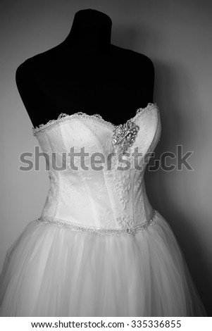 Closeup view of beautiful white luxury wedding female dress with gem and diamonds hanging on black mannequin standing indoor, vertical picture