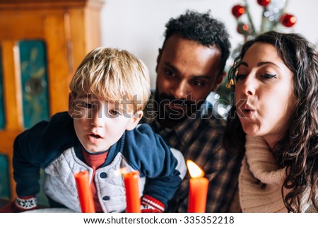 On Christmas Day, a child and a couple of friends have fun in play to blow to extinguish the candles placed on the table where there was the Christmas dinner. Behind them the decorated Christmas tree