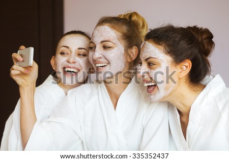 Three young happy women with face masks taking selfi at spa resort. Frenship and wellbeing concept Royalty-Free Stock Photo #335352437