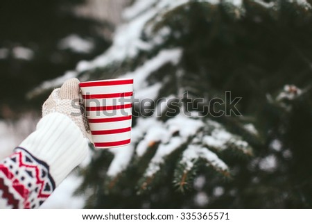 emale hands in mittens holding a cup of tea on a background of a winter forest