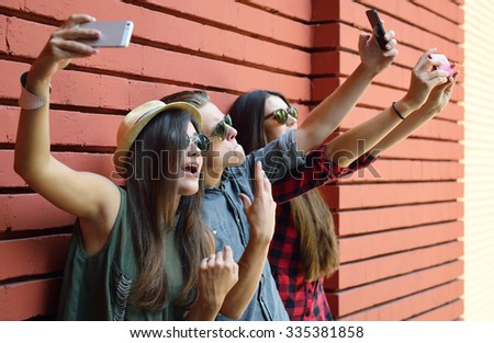 Young people having fun outdoor and making selfie with smart phone against red brick wall. Urban lifestyle, happiness, joy, friends, self photo social network concept. Image toned and noise added.