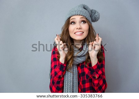 Portrait of a beautiful woman praying with crossed fingers over gray background