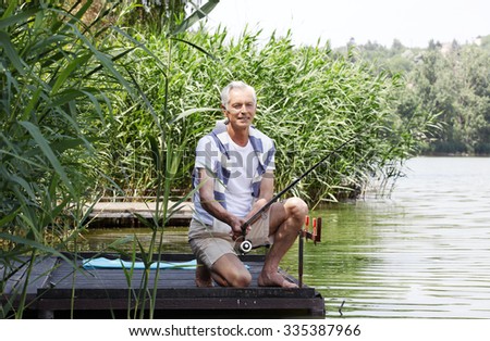 Portrait of senior man sitting at pier at the lakeside and fishing. 