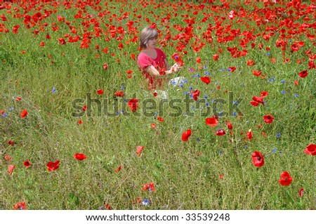 Woman kneels in a field of poppies.  Red poppies fill the meadow as far as the eye can see.