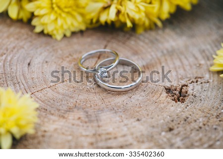 Beautiful two wedding rings, one with a diamond, on a wooden stump with some yellow Chrysanthemum flowers