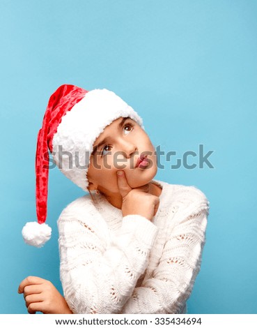 Smiling funny child (kid, girl) in Santa red hat.. Christmas concept. Shooting on blue background