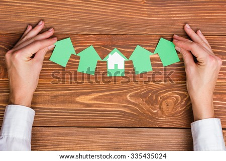 Hands holding paper house figure on wooden background. Real Estate green house Concept. Ecological building. Top view.