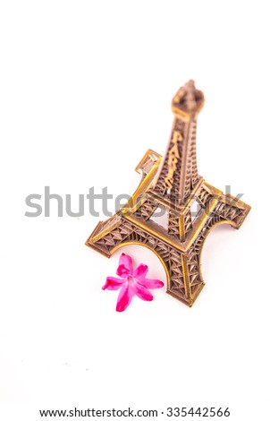 Model of little Eiffel Tower with a pink flower isolated on white. Symbol of Paris and travel in France.