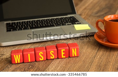 Know (in German) written on a wooden cube in front of a laptop