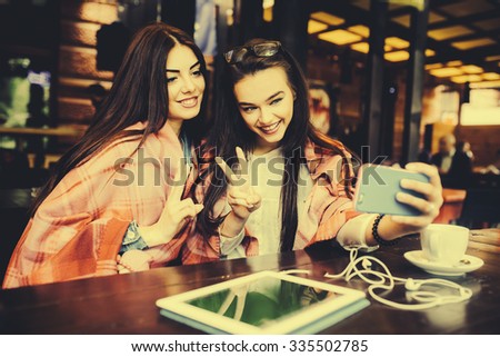 Two young and beautiful girl sitting at the table and doing selfie in the cafe