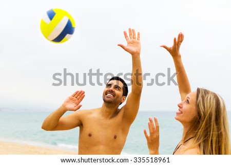 Happy young couple playing volleyball on the beach. Focus on the man
