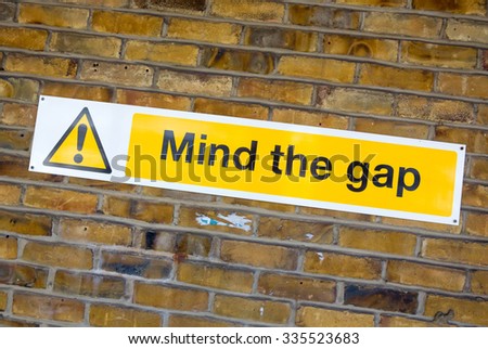 'Mind the Gap' yellow warning sign from the London Underground on a brick wall background