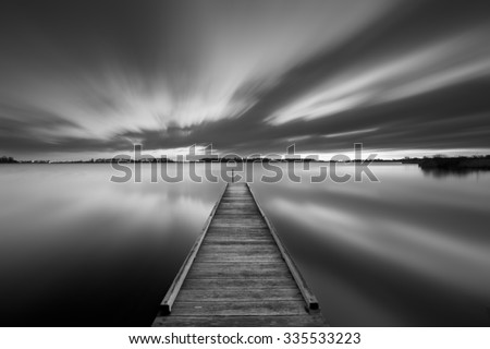 A small jetty on a lake near Amsterdam The Netherlands in black and white. A slow shutter speed was used to see the movement of the clouds in the sky. Photographed at dawn.