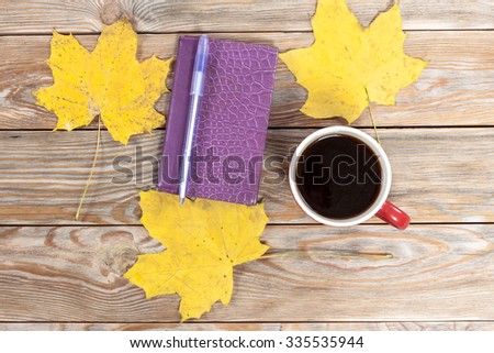 Coffee cup, notebook and autumn leaves on wooden background. Autumn and business background.