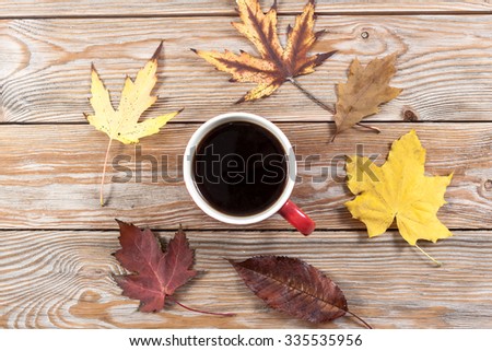 Coffee cup and autumn leaves on wooden background