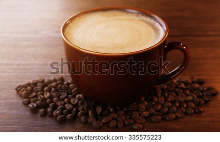 Brown ceramic cup of coffee decorated with roasted beans around on wooden background, close up