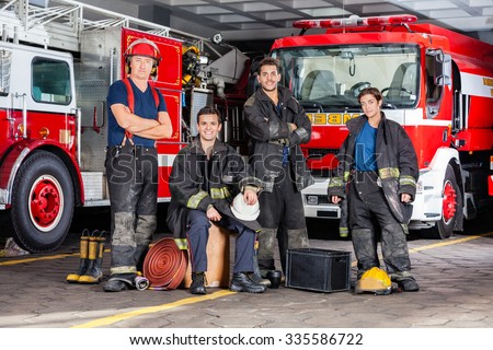 Portrait of confident firefighters with equipment against trucks at fire station Royalty-Free Stock Photo #335586722