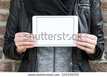 woman standing in front of brick wall holding white tablet with white blank display in her hands