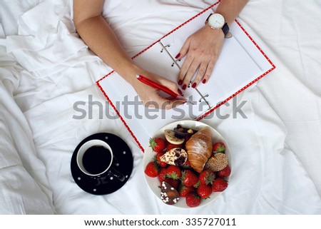 female hands with pen writing on notebook with morning coffee and croissant