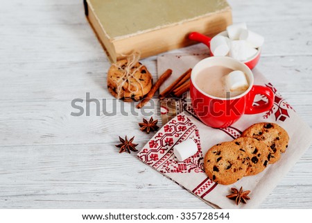 winter mood , cocoa with marshmallows in a red cup , cinnamon and cookies with chocolate on a wooden background
