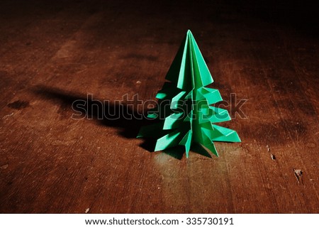 Christmas tree origami on rustic wood background with long shadows.