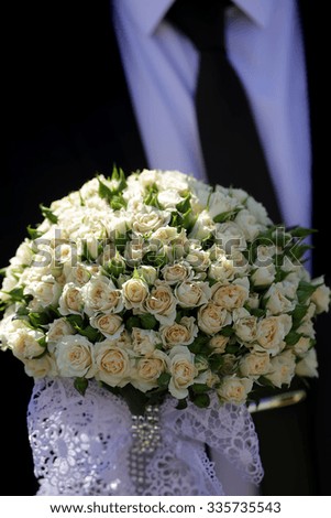 Closeup view of one beautiful fresh bright white yellow big wedding bouquet of rose flowers in hand of bridegroom in black jacket, vertical picture