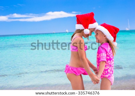 Little adorable girls in red Santa hats on beach tropical vacation 