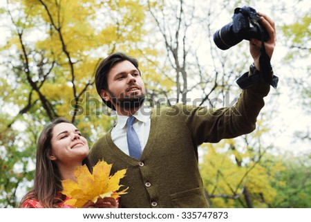 young happy couple making selfie using camera in autumn park