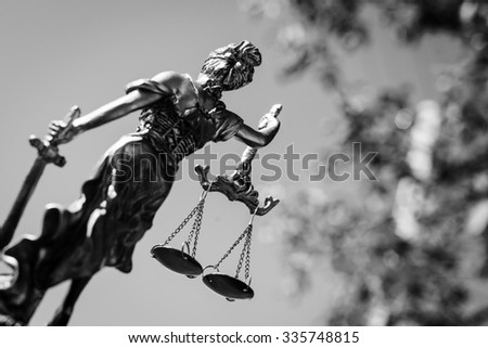 Picture backview of themis sculpture, femida or justice goddess on bright sky and leaves outdoors background. Black and white photography