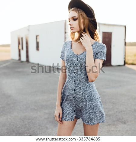 Fashionable girl in a dress and hat posing outdoors on a sunny day
