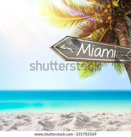 Miami wooden sign and blurry exotic beach background. Tropical landscape with coconut palm tree and white sand beach. Paradise design banner background.