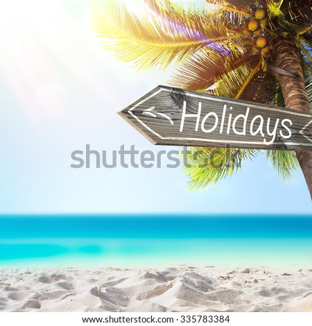Holidays wooden sign and blurry exotic beach background. Tropical landscape with coconut palm tree and white sand beach. Paradise design banner background.