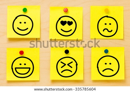 Hand drawing emoticons on six yellow postit notes affixed by colored pins on a wooden board