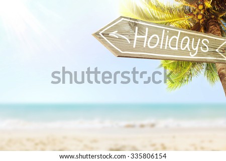 Holidays wooden sign and blurry exotic beach background. Tropical landscape with coconut palm tree and white sand beach. Paradise design banner background.