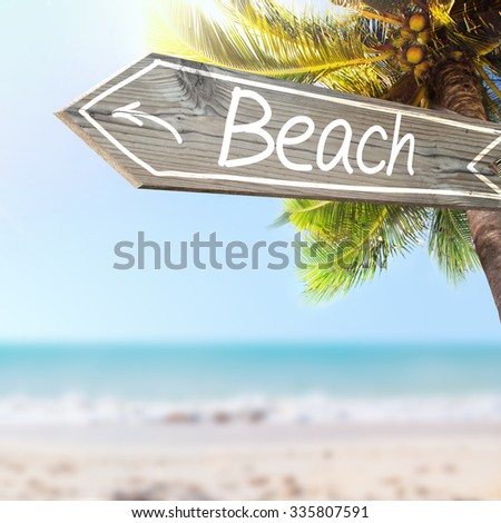 Beach wooden sign and blurry exotic beach background. Tropical landscape with coconut palm tree and white sand beach. Paradise design banner background.